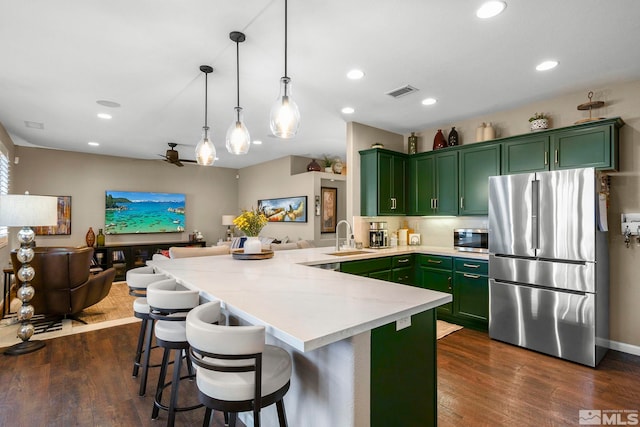 kitchen featuring stainless steel appliances, dark wood-type flooring, kitchen peninsula, pendant lighting, and green cabinetry