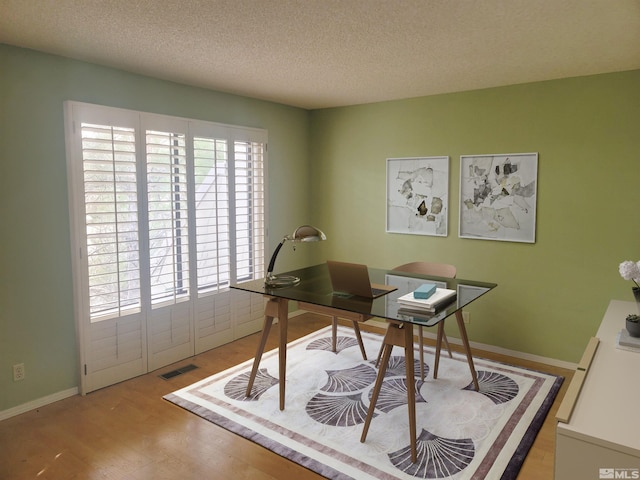 home office featuring light wood-type flooring and a textured ceiling