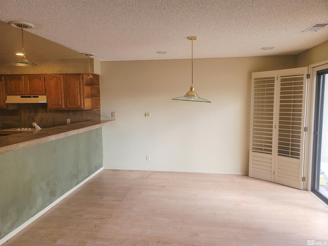 kitchen with a textured ceiling, kitchen peninsula, light hardwood / wood-style floors, and decorative light fixtures