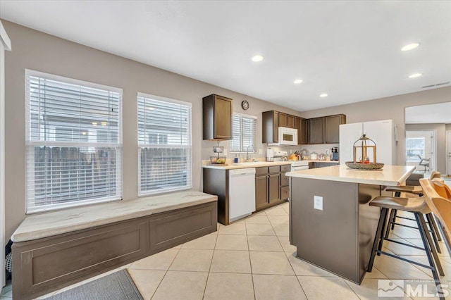 kitchen with a kitchen bar, white appliances, sink, light tile patterned floors, and a center island