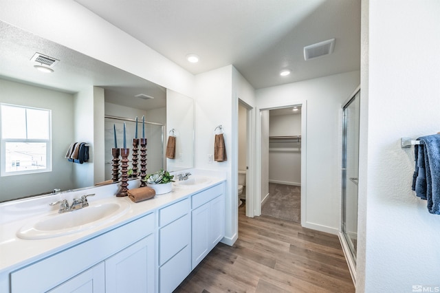 bathroom featuring toilet, wood-type flooring, a shower with door, and vanity