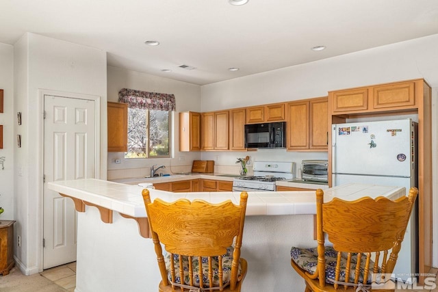 kitchen featuring a kitchen breakfast bar, white gas range, tile counters, and sink