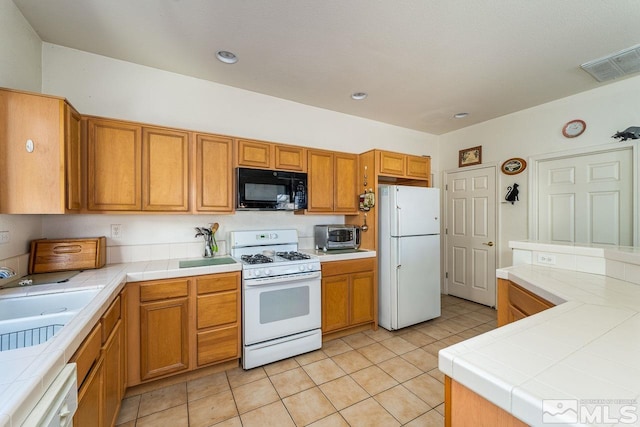 kitchen featuring tile counters, white appliances, sink, and light tile patterned floors