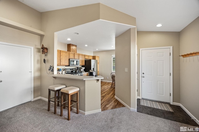 kitchen featuring kitchen peninsula, dark colored carpet, stainless steel appliances, and a breakfast bar area