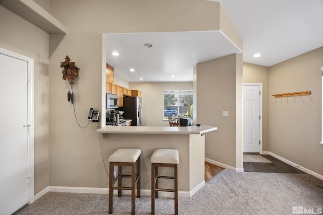 kitchen featuring a kitchen bar, appliances with stainless steel finishes, kitchen peninsula, light brown cabinets, and carpet floors