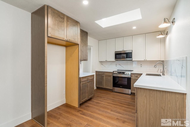 kitchen with backsplash, a skylight, stainless steel appliances, sink, and white cabinetry