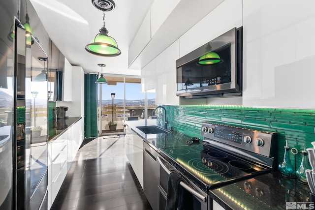 kitchen with pendant lighting, dark stone counters, white cabinets, sink, and appliances with stainless steel finishes