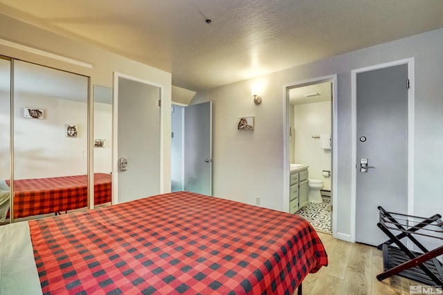 bedroom with ensuite bath, a closet, and light wood-type flooring