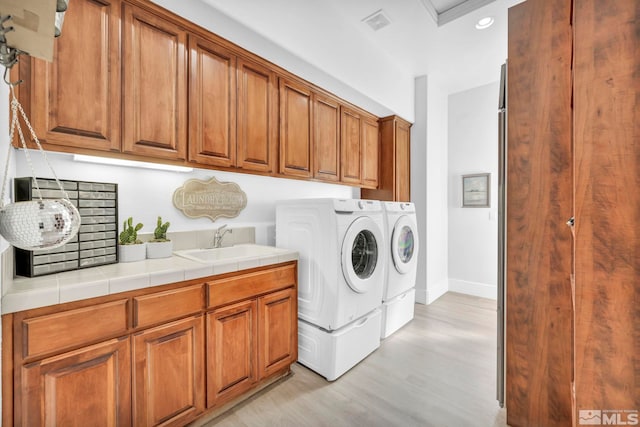 washroom with cabinets, sink, washer and dryer, and light hardwood / wood-style flooring