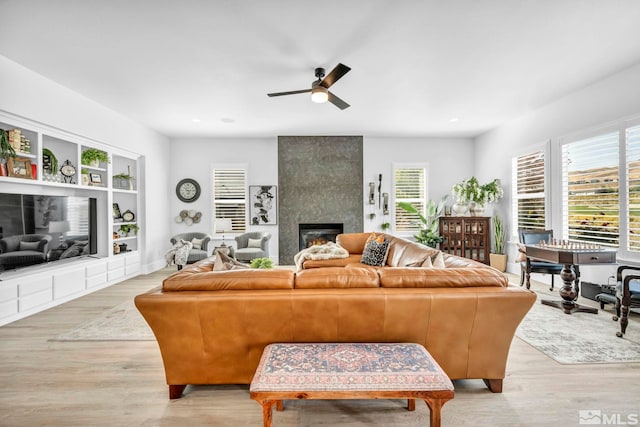 living room with a fireplace, built in shelves, light hardwood / wood-style flooring, and ceiling fan