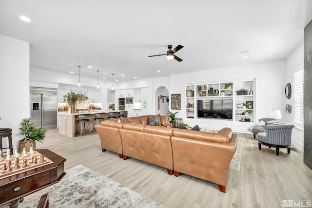 living room featuring built in shelves, light wood-type flooring, and ceiling fan