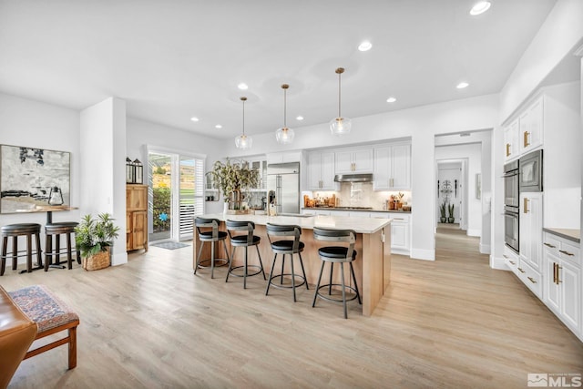 kitchen with stainless steel appliances, a kitchen island with sink, white cabinets, and hanging light fixtures