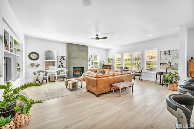 living room with a fireplace, light wood-type flooring, and ceiling fan