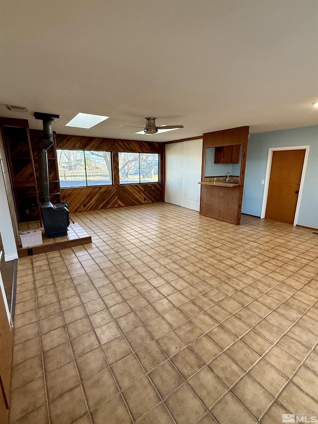 unfurnished living room with wood walls, ceiling fan, and a wood stove