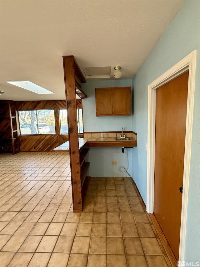 kitchen with a skylight, kitchen peninsula, light tile patterned floors, a breakfast bar, and sink