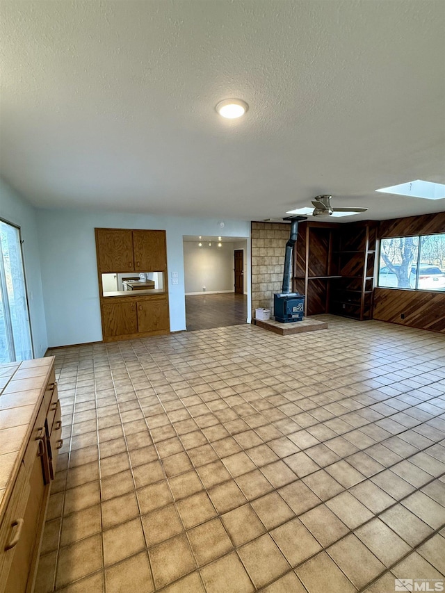 unfurnished living room featuring a textured ceiling, light tile patterned flooring, and a wood stove