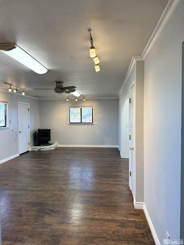 unfurnished living room featuring ceiling fan, a wood stove, crown molding, and dark hardwood / wood-style floors