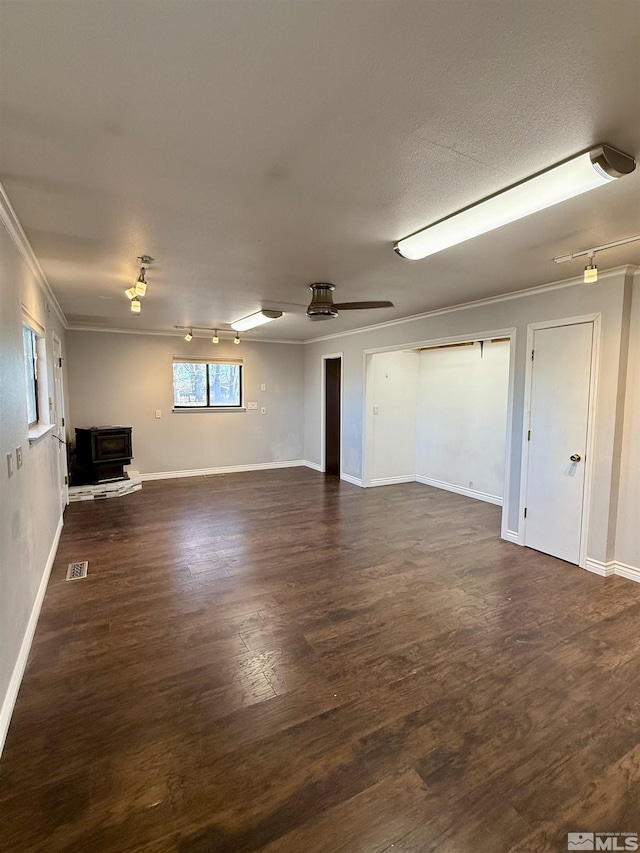 basement featuring crown molding, ceiling fan, dark wood-type flooring, a wood stove, and a textured ceiling