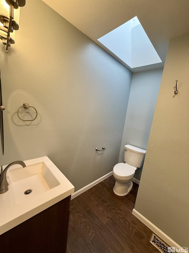 bathroom featuring a skylight, toilet, vanity, and hardwood / wood-style flooring