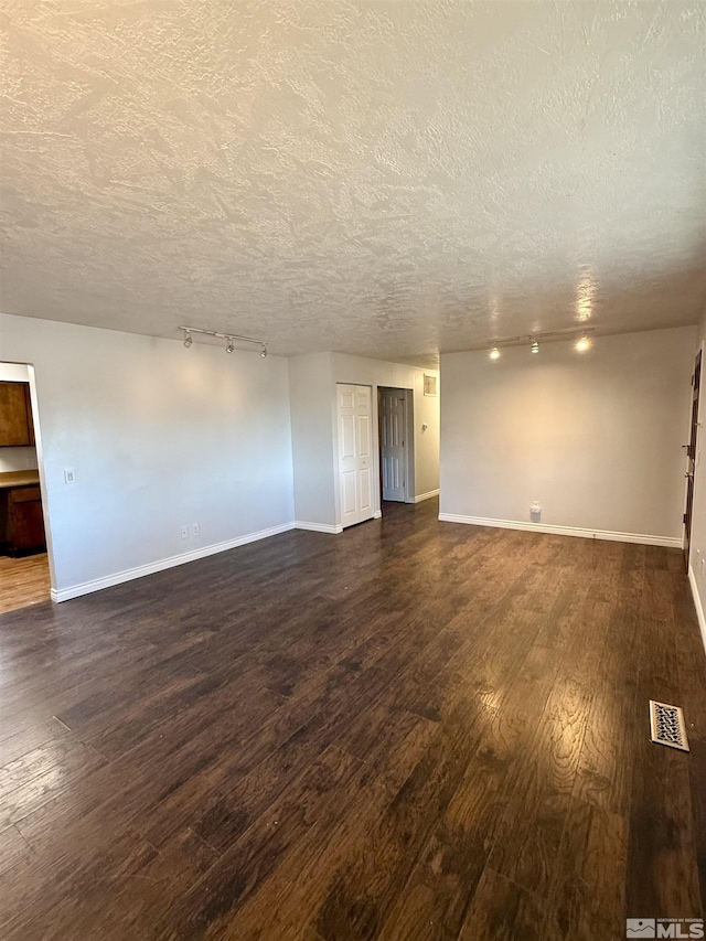 spare room with track lighting, a textured ceiling, and dark hardwood / wood-style floors