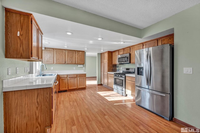 kitchen with a textured ceiling, stainless steel appliances, sink, light hardwood / wood-style floors, and tile counters