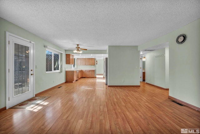 unfurnished living room featuring a textured ceiling, light wood-type flooring, and ceiling fan