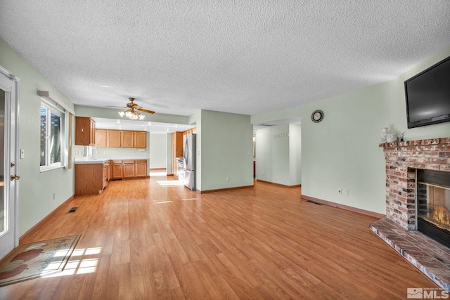 unfurnished living room with ceiling fan, sink, a textured ceiling, a fireplace, and light wood-type flooring