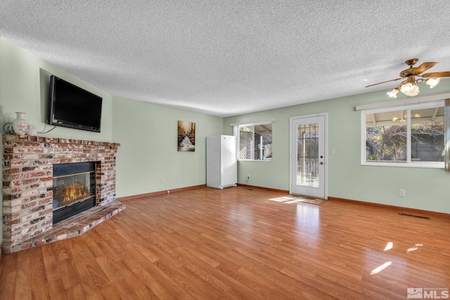 unfurnished living room with a fireplace, light hardwood / wood-style floors, ceiling fan, and a healthy amount of sunlight