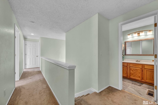 hallway with light carpet, sink, and a textured ceiling