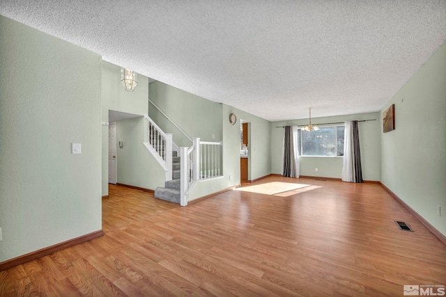 unfurnished living room featuring light hardwood / wood-style flooring, a textured ceiling, and a notable chandelier