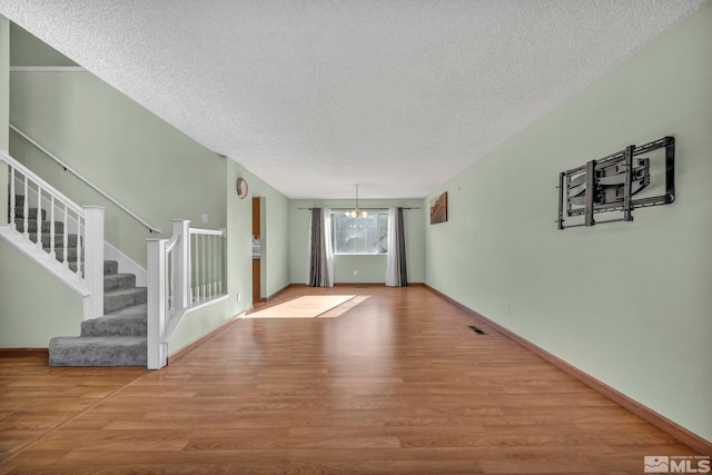 unfurnished living room featuring wood-type flooring, a textured ceiling, and an inviting chandelier