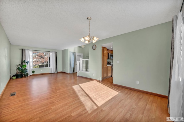 unfurnished living room featuring a textured ceiling, light hardwood / wood-style flooring, and a notable chandelier