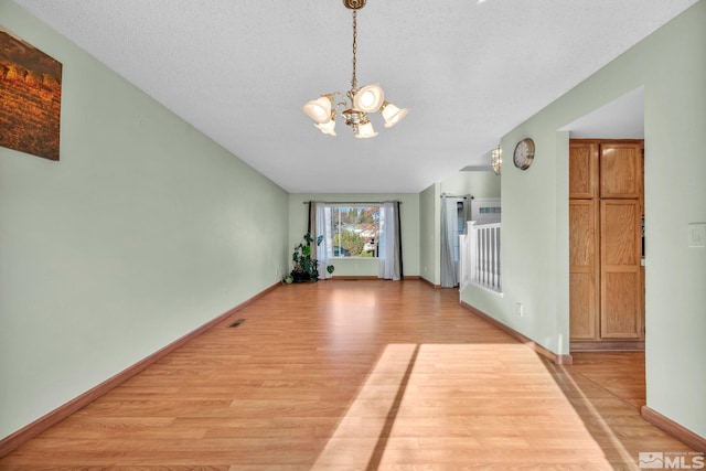 interior space with light wood-type flooring, a textured ceiling, and an inviting chandelier