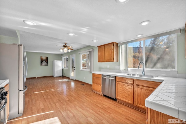 kitchen featuring appliances with stainless steel finishes, ceiling fan, sink, tile countertops, and light hardwood / wood-style flooring