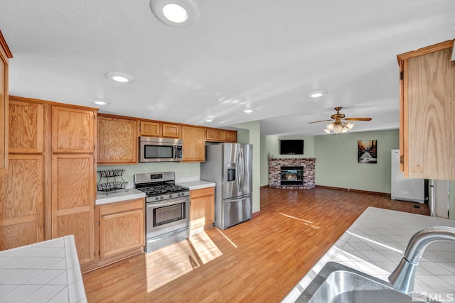 kitchen featuring tile countertops, ceiling fan, light wood-type flooring, a fireplace, and stainless steel appliances