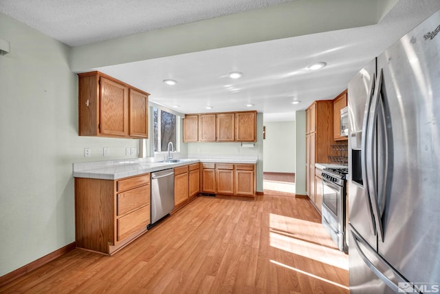 kitchen featuring sink, tile countertops, a textured ceiling, appliances with stainless steel finishes, and light wood-type flooring