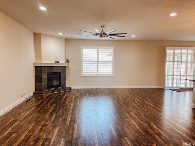 unfurnished living room featuring a tiled fireplace, ceiling fan, and dark hardwood / wood-style floors