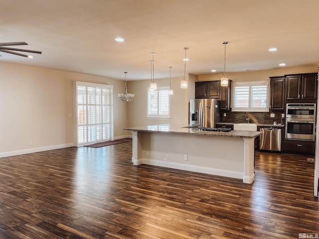 kitchen with stainless steel appliances, dark hardwood / wood-style floors, tasteful backsplash, an island with sink, and light stone countertops