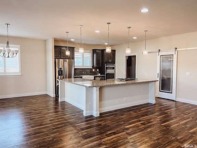 kitchen with a large island, a barn door, stainless steel appliances, light stone counters, and dark brown cabinets