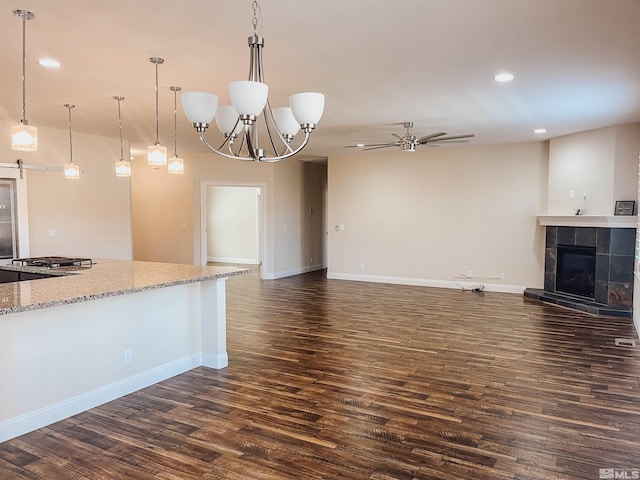 unfurnished living room featuring ceiling fan with notable chandelier, a tile fireplace, and dark hardwood / wood-style floors