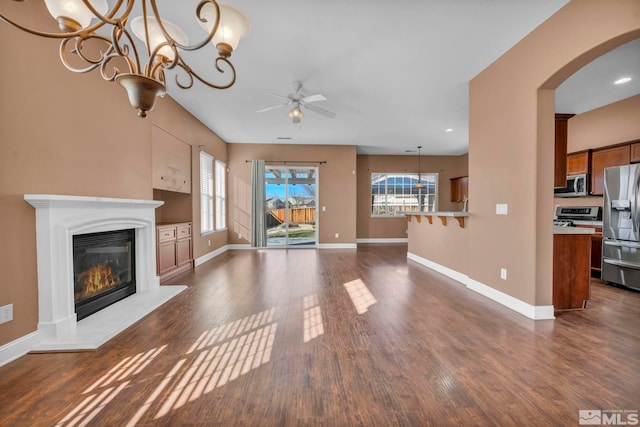 unfurnished living room featuring ceiling fan with notable chandelier, dark hardwood / wood-style flooring, and plenty of natural light