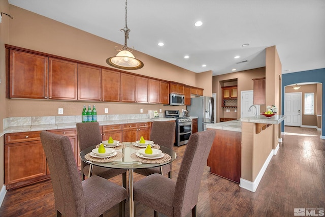 kitchen with dark wood-type flooring, decorative light fixtures, a breakfast bar area, appliances with stainless steel finishes, and sink