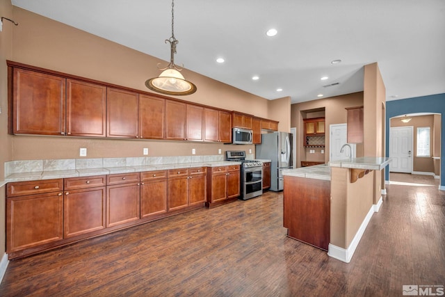 kitchen featuring sink, appliances with stainless steel finishes, decorative light fixtures, a kitchen bar, and dark wood-type flooring