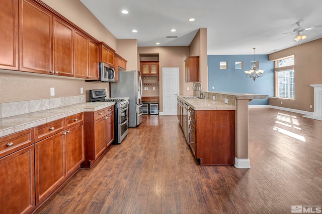 kitchen with dark wood-type flooring, pendant lighting, a breakfast bar area, ceiling fan with notable chandelier, and appliances with stainless steel finishes