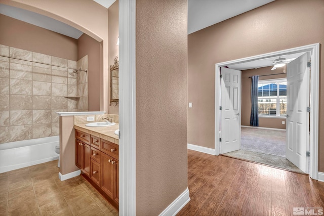 full bathroom featuring toilet, tiled shower / bath, hardwood / wood-style floors, ceiling fan, and vanity