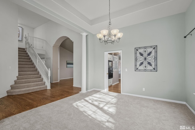 empty room with an inviting chandelier, dark colored carpet, and ornate columns