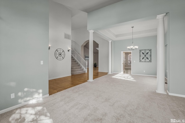 unfurnished living room featuring a notable chandelier, carpet, and decorative columns