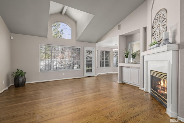 unfurnished living room featuring vaulted ceiling with beams, a tile fireplace, a chandelier, and hardwood / wood-style flooring