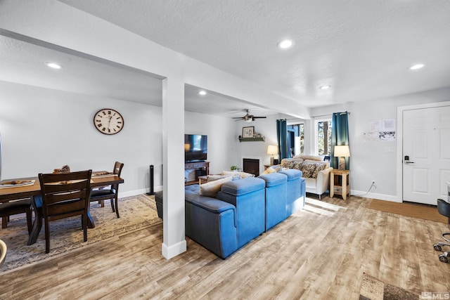 living room with a textured ceiling, ceiling fan, and light wood-type flooring