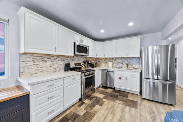 kitchen with stainless steel appliances, sink, white cabinetry, tasteful backsplash, and light hardwood / wood-style flooring